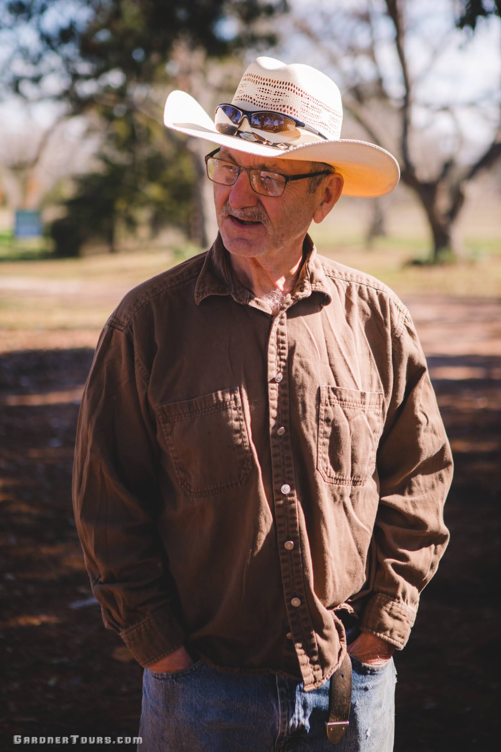 Older cowboy wearing a cowboy hat and brown shirt talking to someone under the sun on his ranch outside of Centerville, Texas.