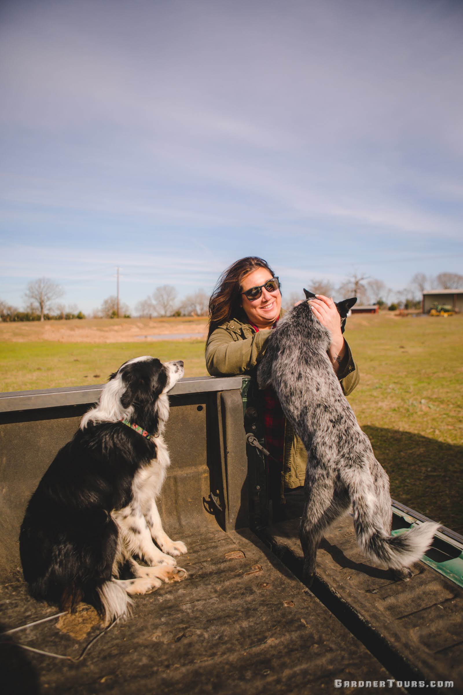 A woman pets two friendly dogs in the back of a green truck on a ranch outside of Centerville, Texas.