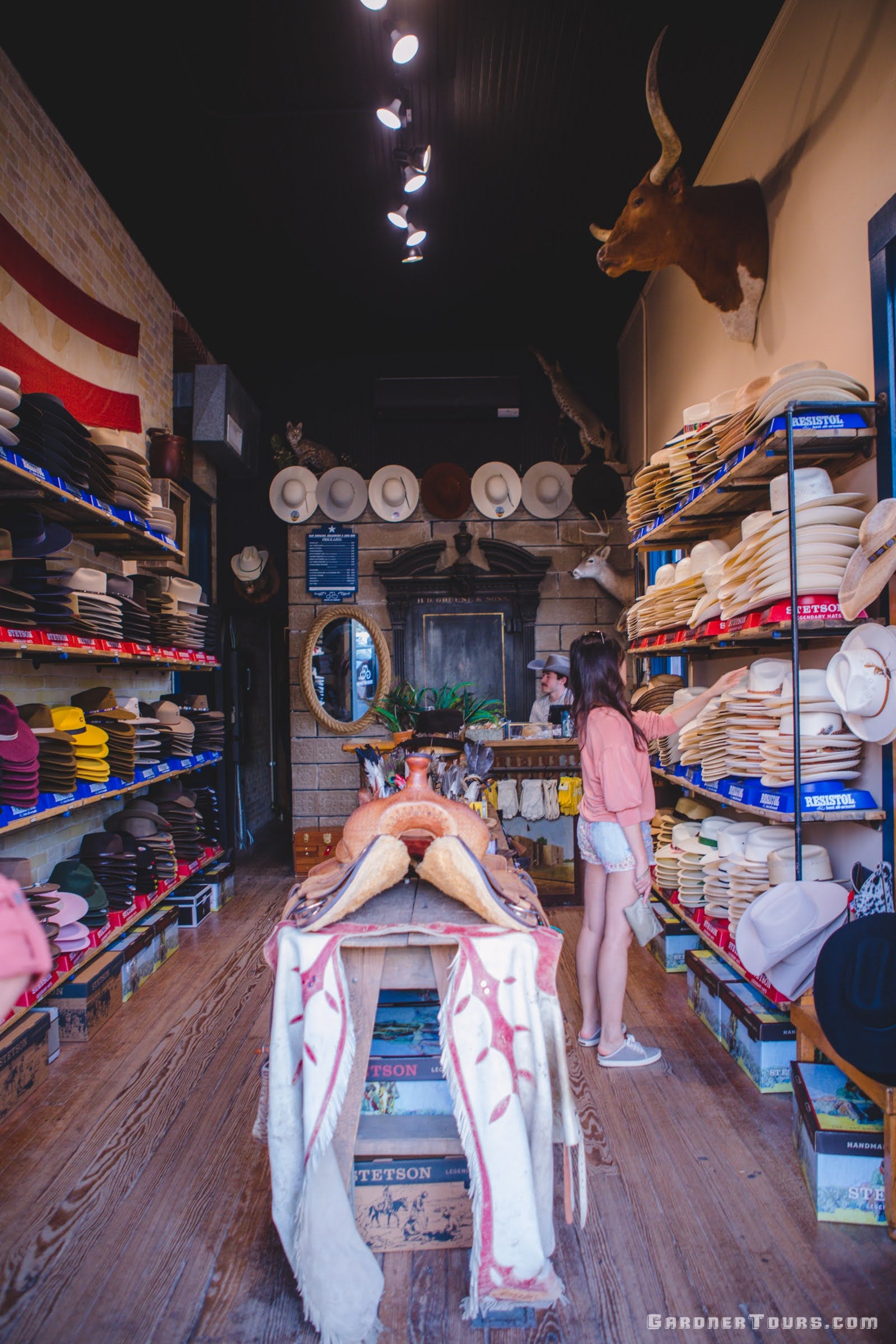 A young woman in tan shorts and a pink shirt shops for a cowboy hat, boots, and other western wear at Gruene Hat Company in Gruene, Texas.