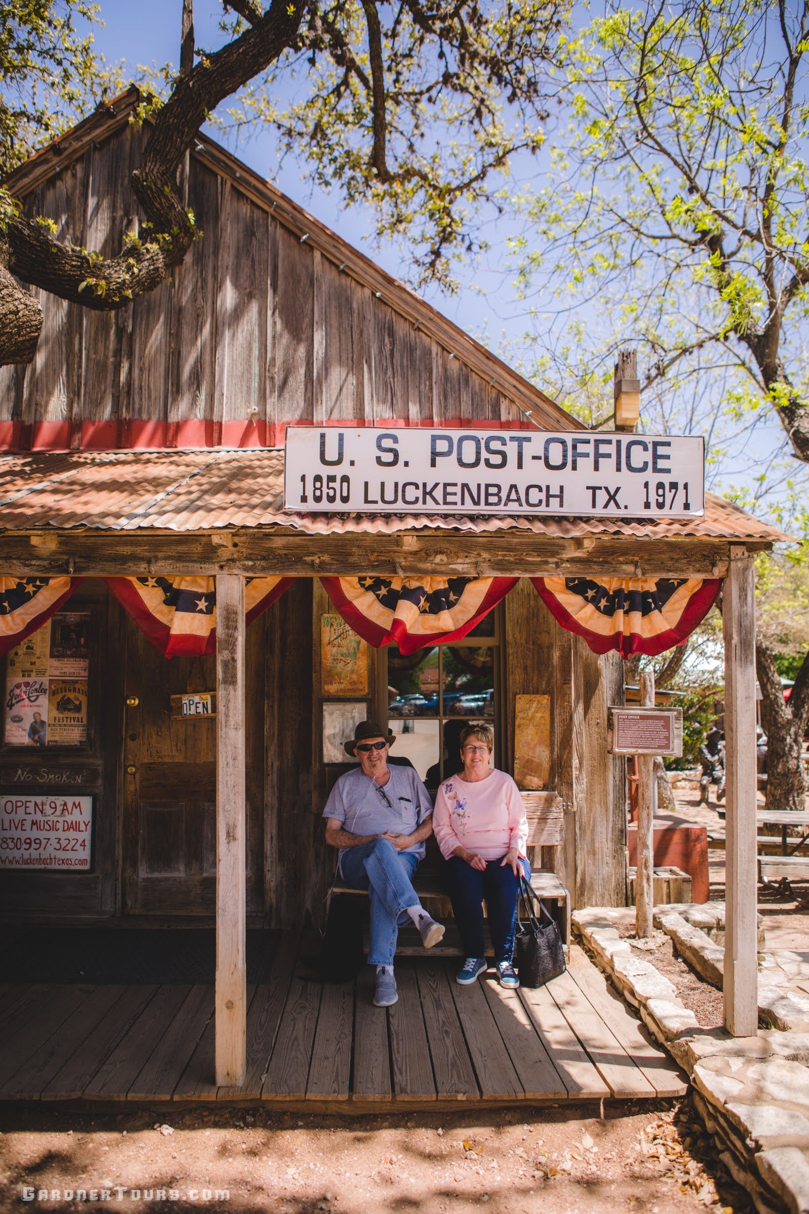 an elderly couple sit on the front porch bench of the luckenbach texas post office
