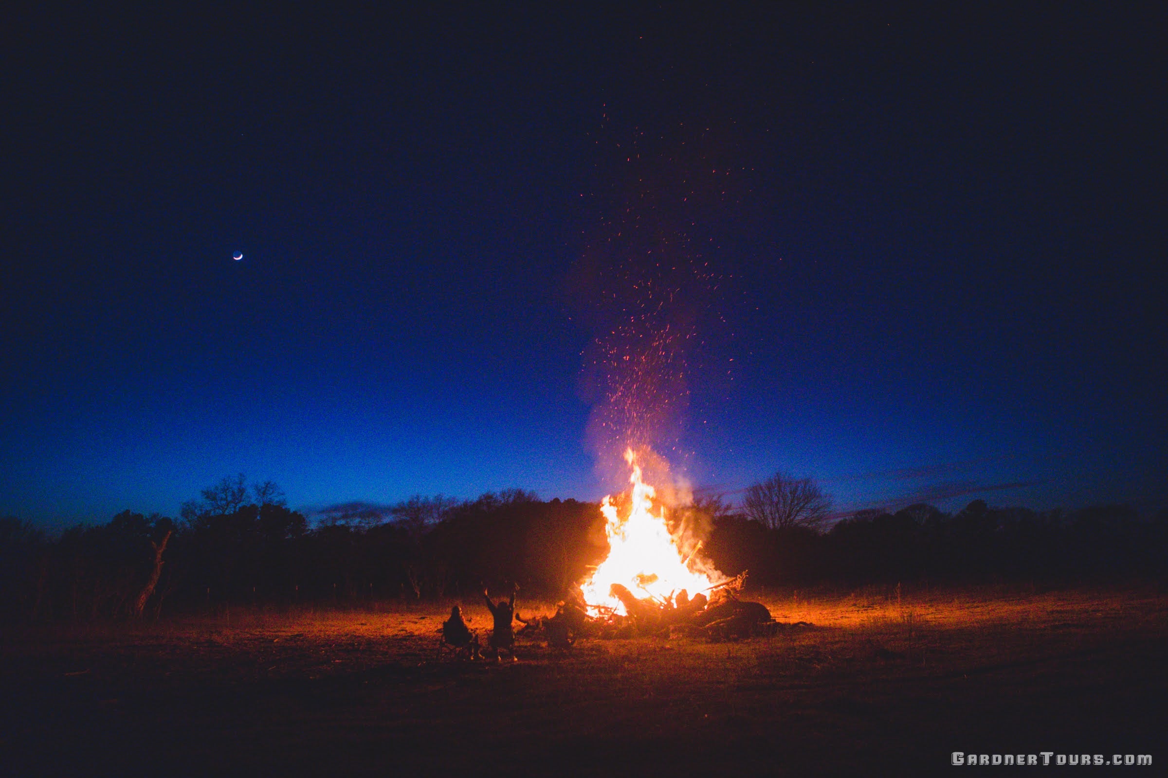 Guests enjoying a large evening bonfire under a starry sky on the farm property after a Texas hog hunt.