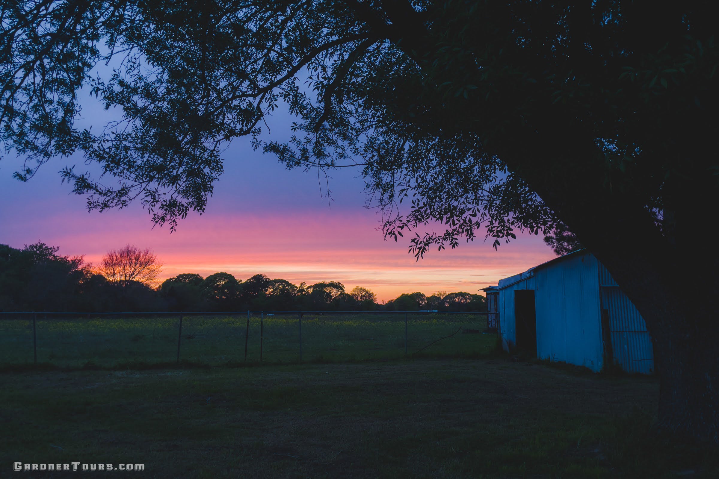 Vibrant pink and orange Texas sunset over the open pasture and barn at the Gardner family farm and ranch near Centerville, Texas.