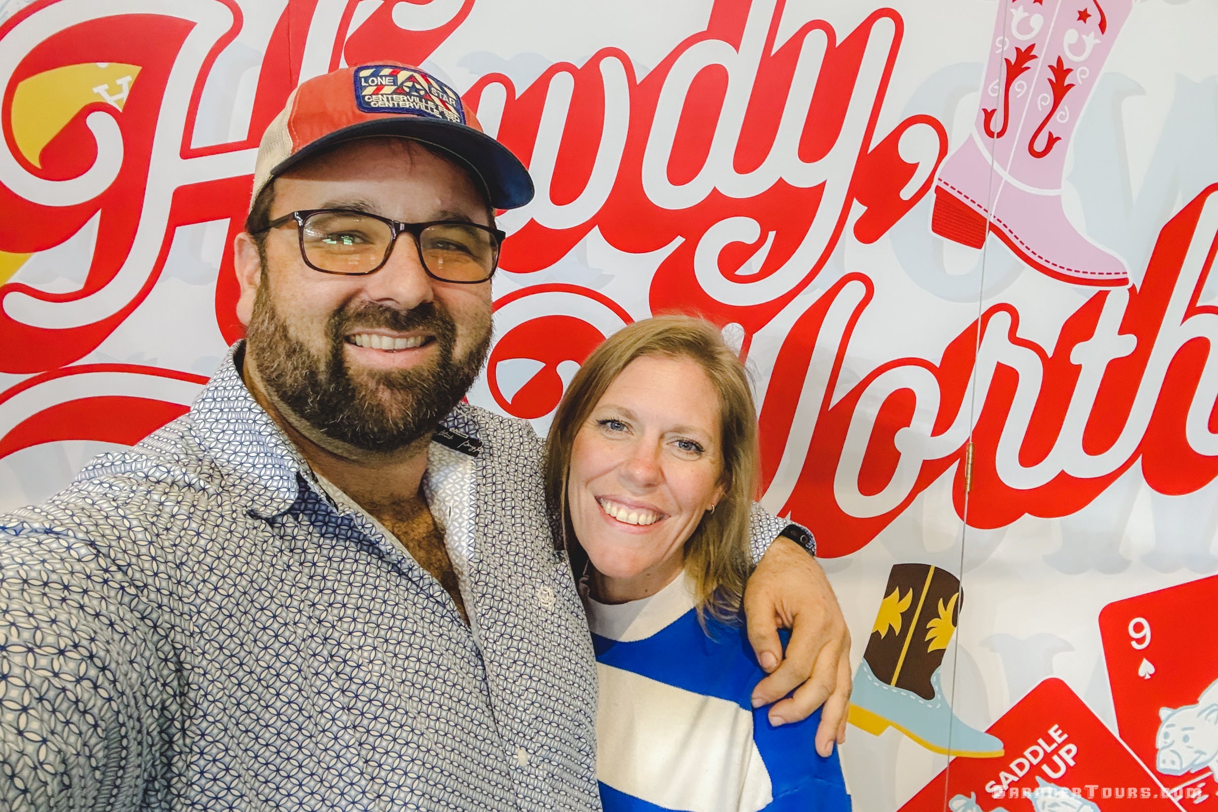 Two people posing in front of a 'Howdy, Fort Worth' themed backdrop with cowboy elements.