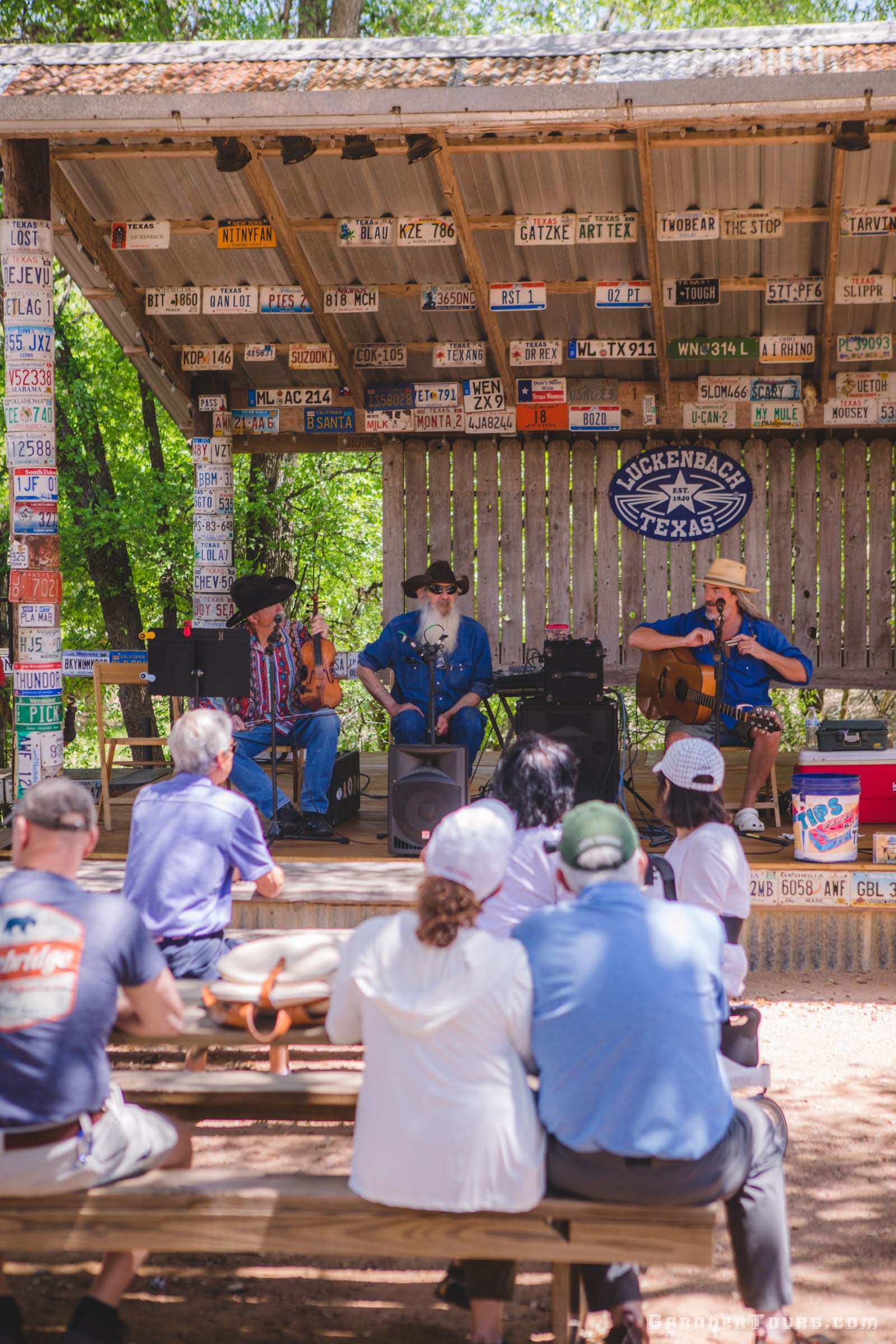 A group of people sit on benches while listening to live music in Luckenbach, Texas.