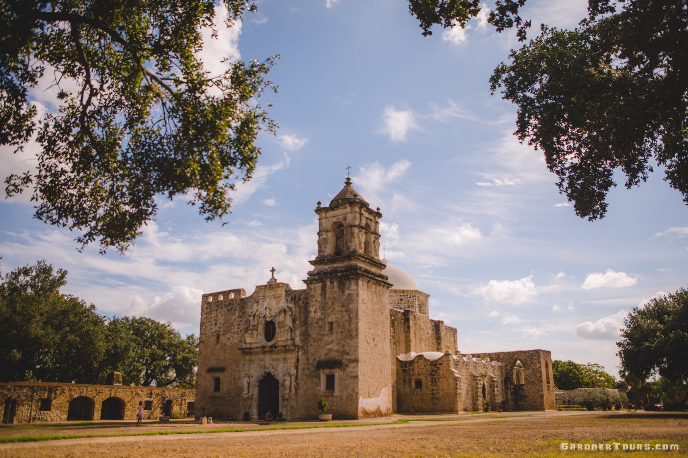 Beautiful view of the historic Mission San José in San Antonio from under the oak trees on a day with blue skies and few clouds.