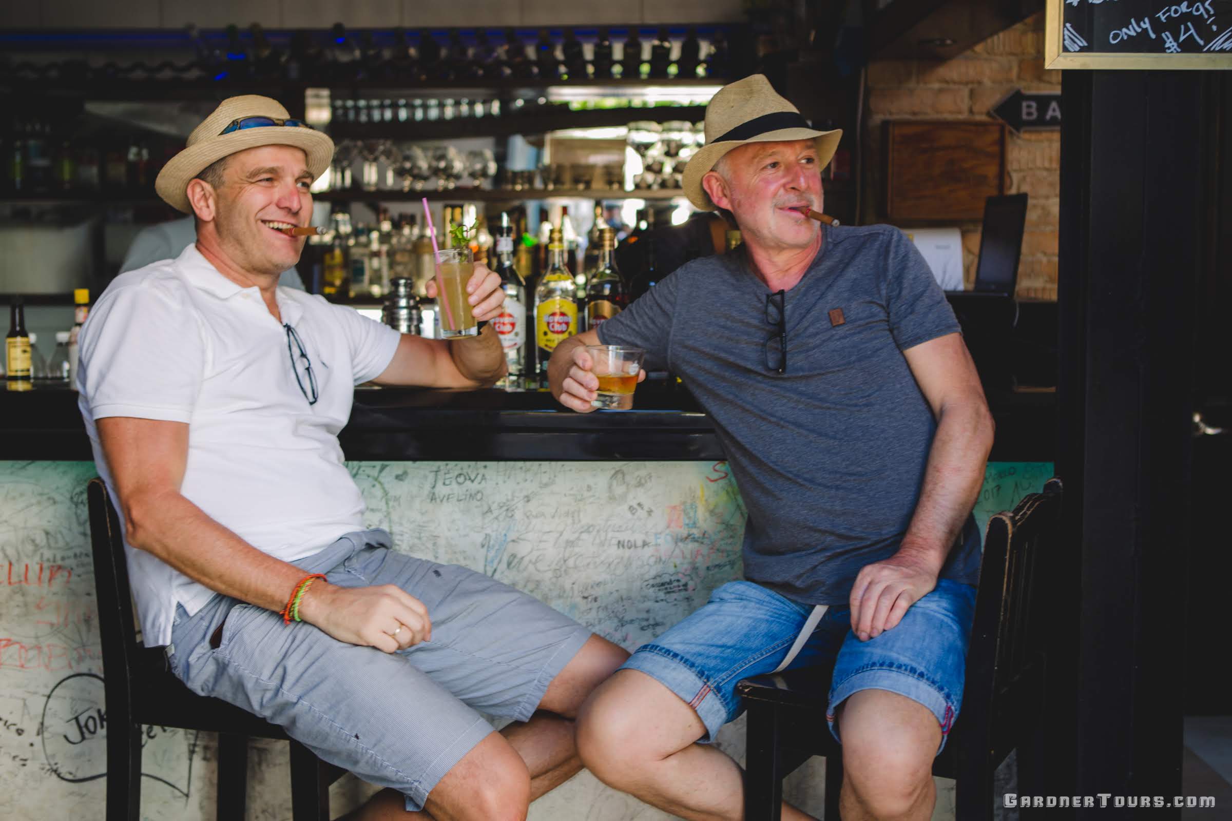 Two middle aged White Men sit at a bar Enjoying Cuban Cigars and drinks In Havana Cuba