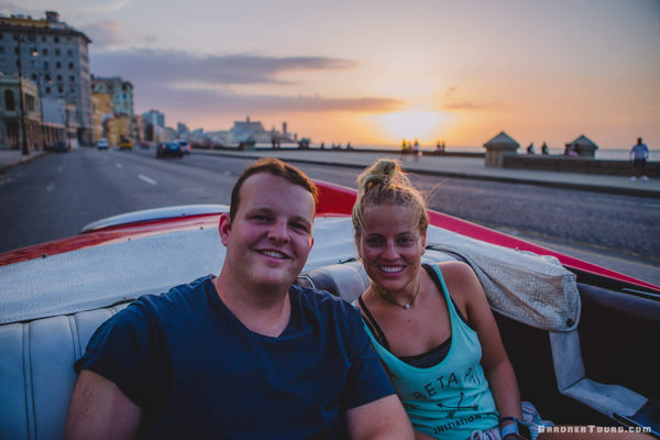 Man and Woman Cruising down the Malecon at sunset in Havana on Classic Car Tour in Classic American Car