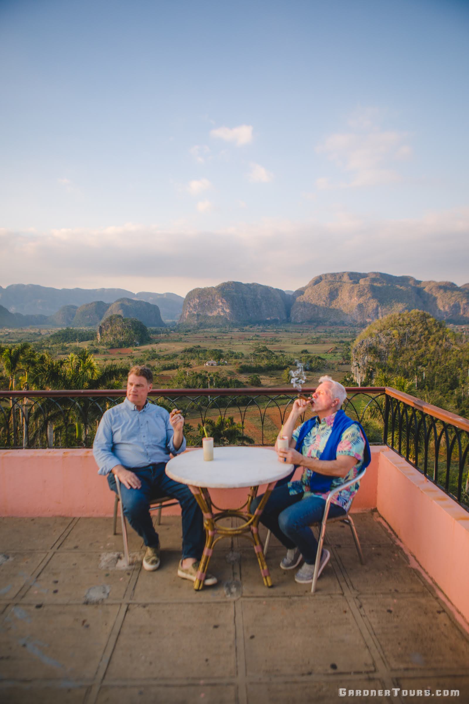 Two Men sitting at a table and Smoking Cigars and Having Drinks at the Viewpoint over the Vinales Valley in Cuba